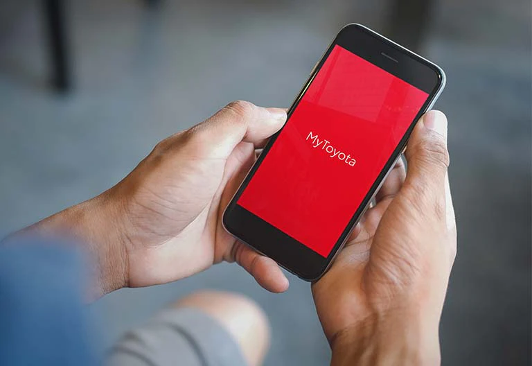 Toyota-appen MyToyotas logotyp på en mobilskärm som hålls av två händer