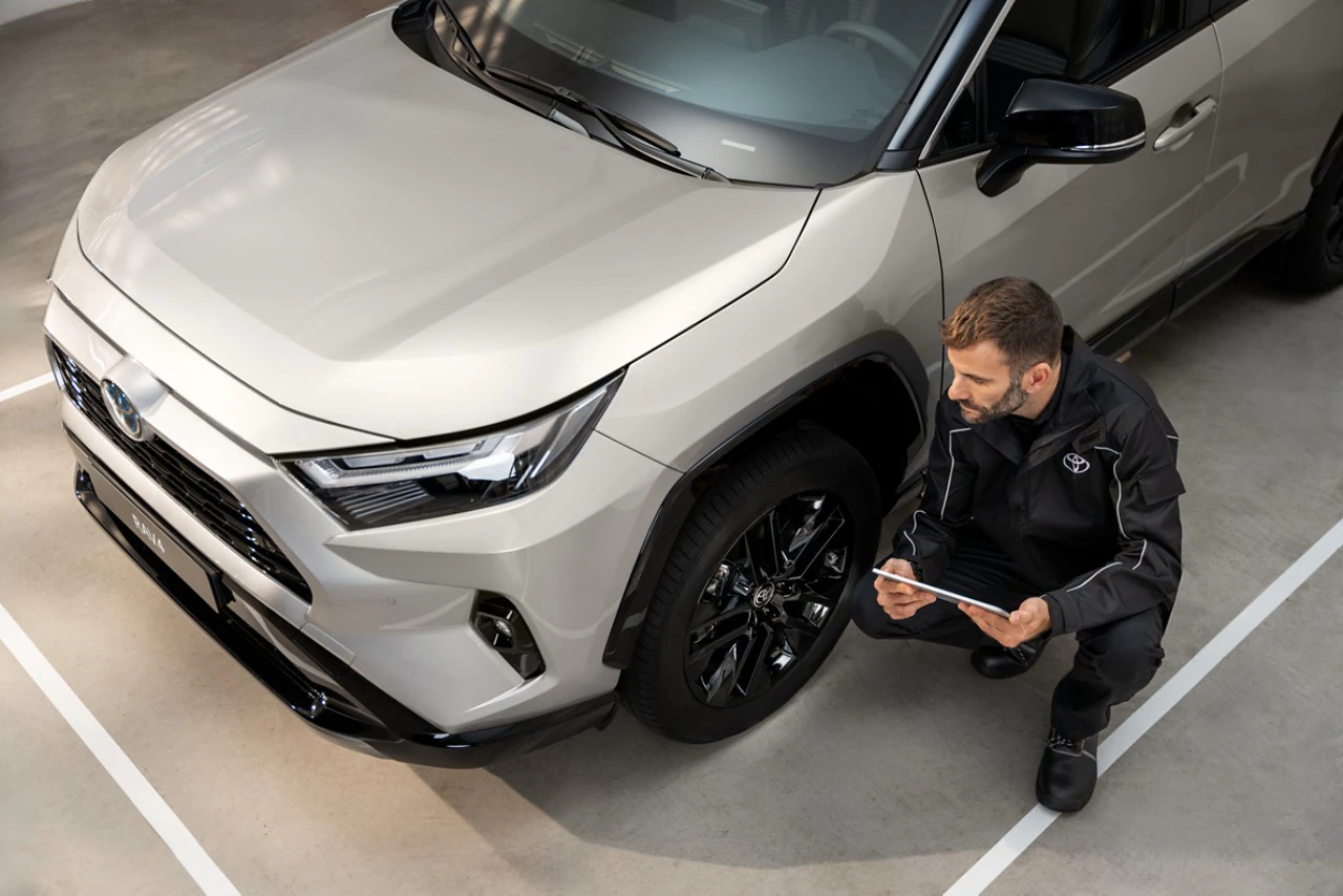 En servicetekniker som sitter på huk framför hjulen på en vit Toyota