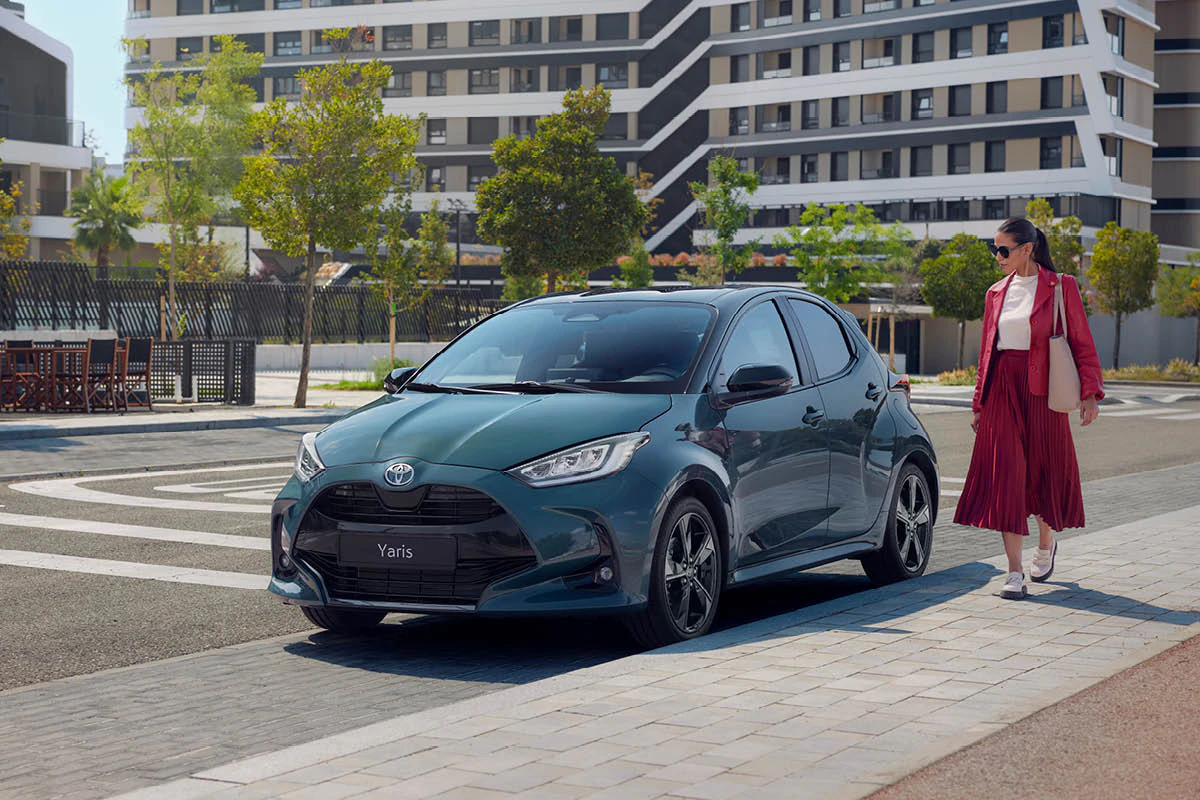 En kvinna står vid en parkerad Toyota Yaris.