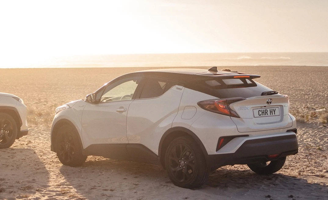 En vit Toyota C-HR som står parkerad i solen på en sandstrand