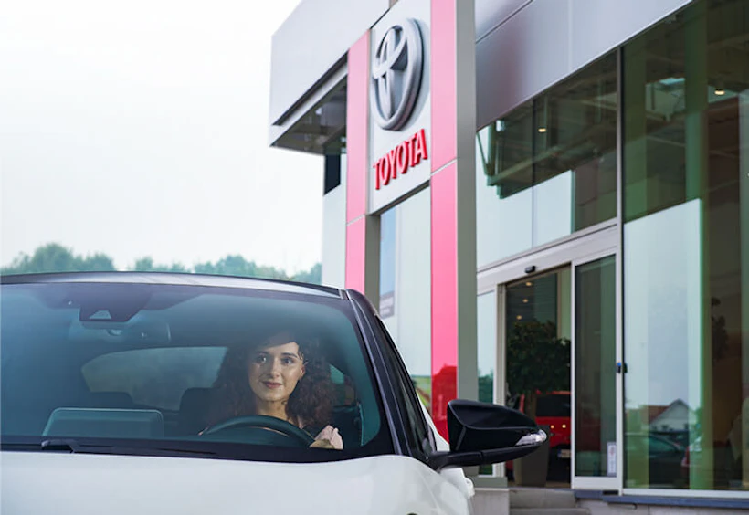En kvinna som sitter i en bil framför en Toyota-anläggning
