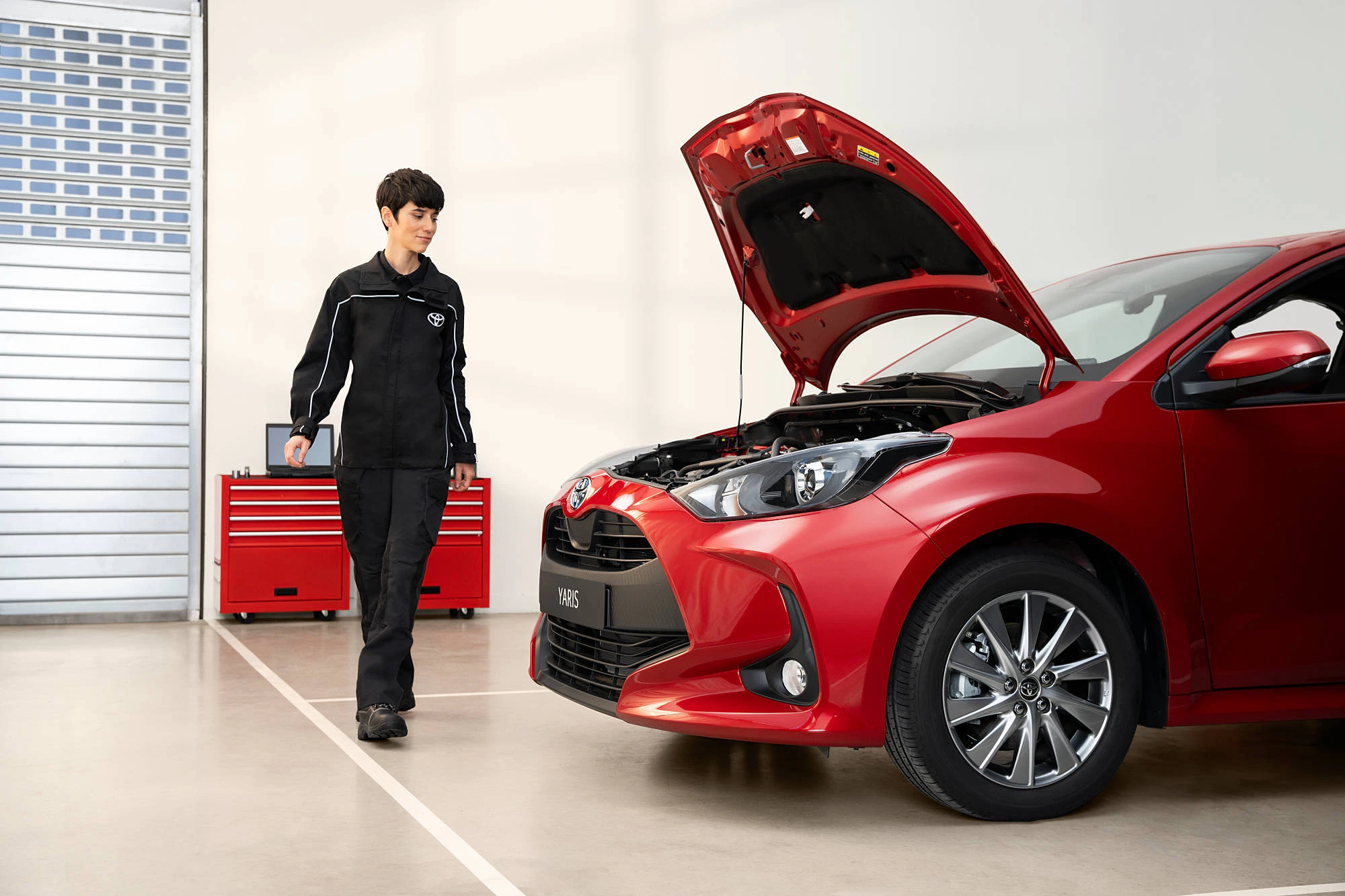 En kvinnlig servicetekniker som står framför en röd Toyota Yaris som har öppen motorhuv