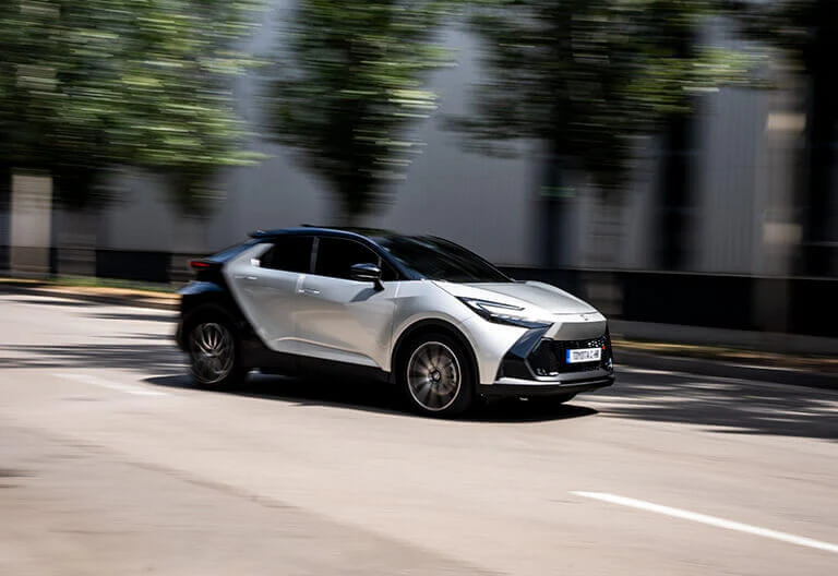 En grå Toyota C-HR som åker på en väg där det är soligt